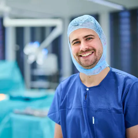 Ein auszubildender Operationstechniker steht in OP-Kleidung in Operationsraum und wendet das Erlernte in der Praxis an 